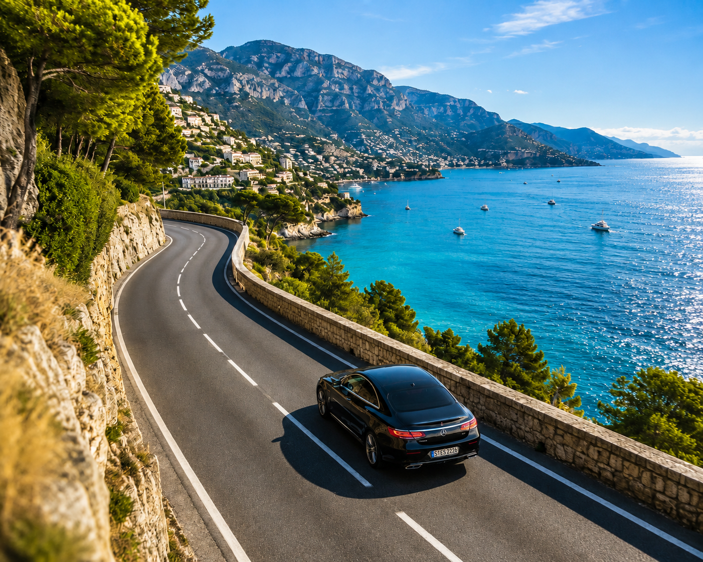 A black grand touring car travelling along a Mediterranean coastal road on the French Riviera.
